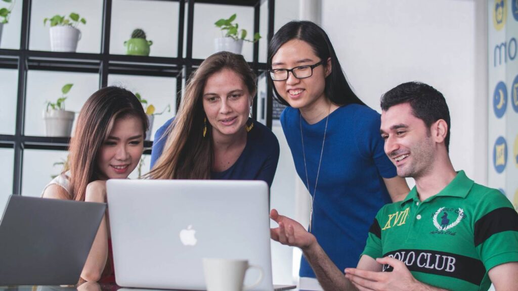 Four office workers laughing together while looking at a laptop 