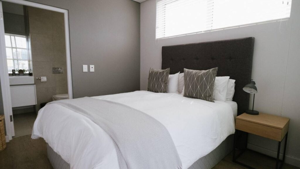 A photo of a hotel sleeping room with a comfortable bed, next to the bathroom door 