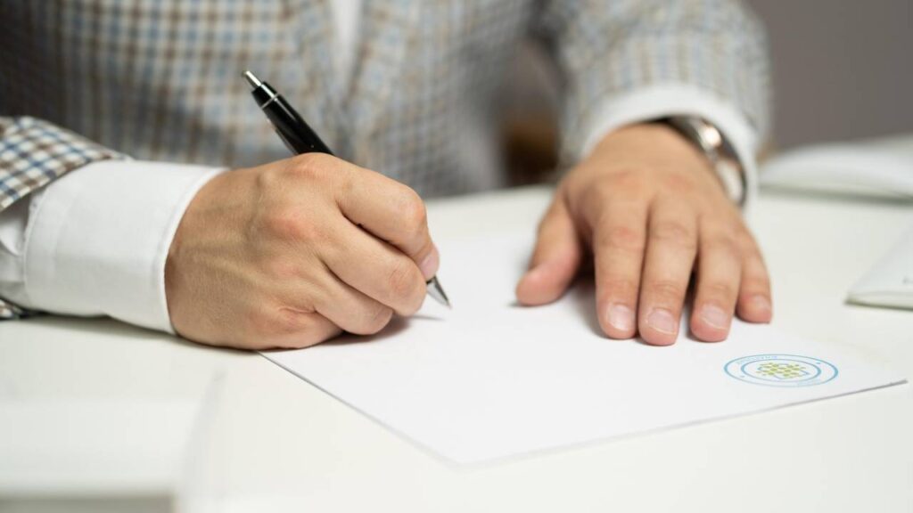 Man in a white suit signing a certification document
